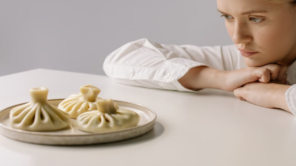 A woman in a white shirt gazes at a plate of traditional Georgian khinkali dumplings.